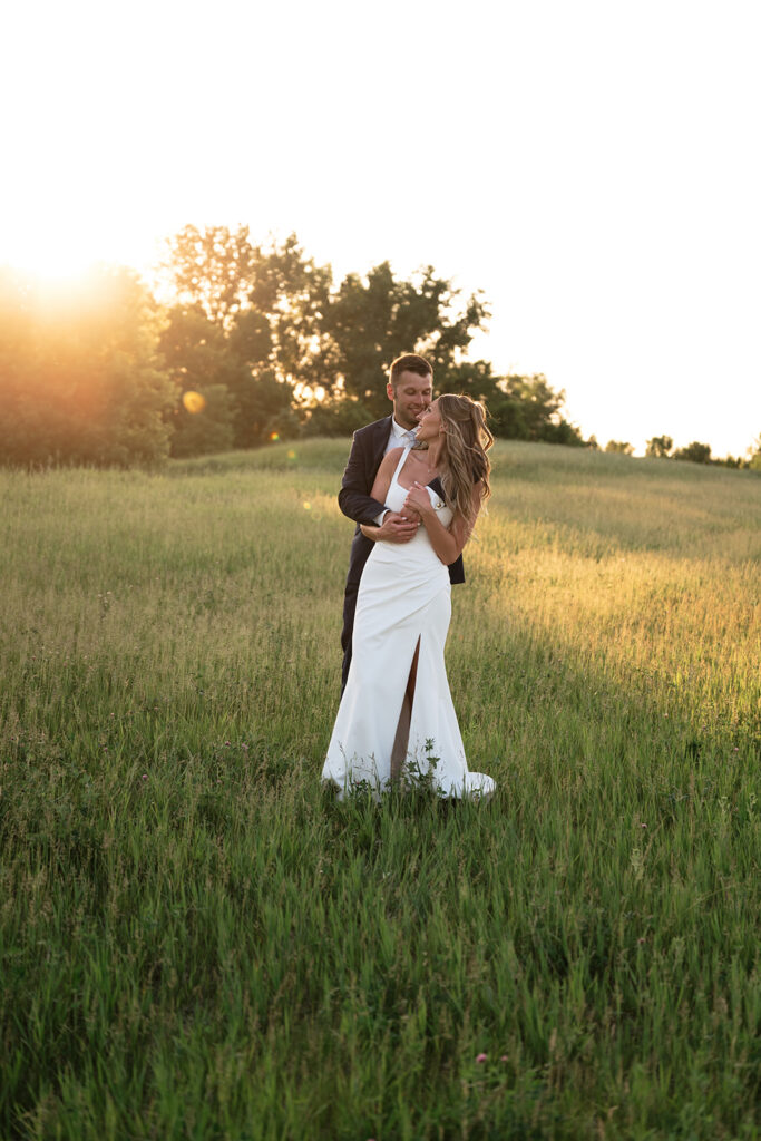 Bride and groom embracing in a grassy field during golden hour at their Freeport, Minnesota wedding