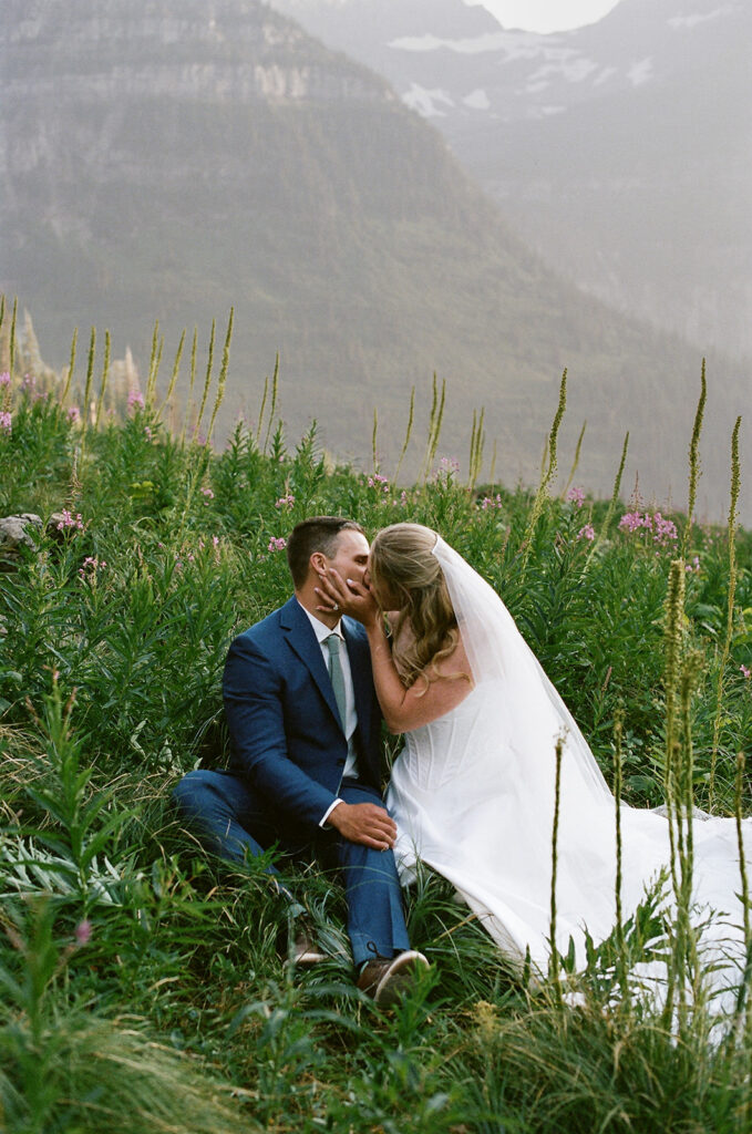 bride and groom sitting in a wildflower patch in glacier national park